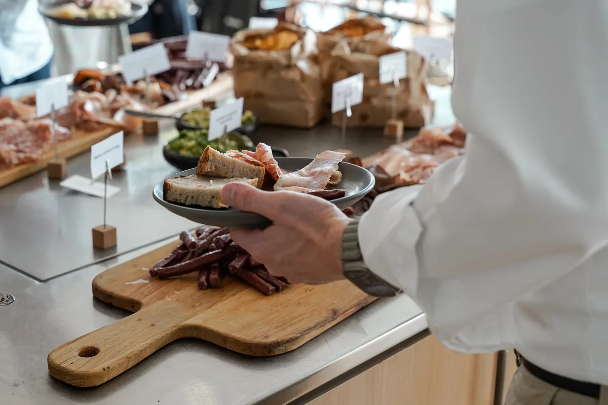 Gæst tager charcuteri fra en buffet med skilte ved hver ret