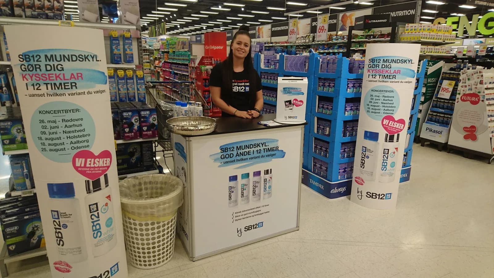 Promotionmedarbejder ved en stand i et supermarked med produkter og skiltning